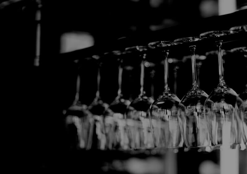 A grayscale photo of wine glasses hanging from a rack.