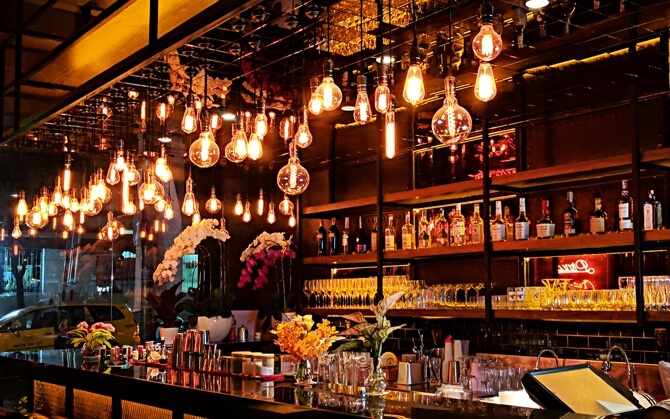 A swanky looking bar with shelves of liquor bottles and various glassware, lit by funky looking bulbs.