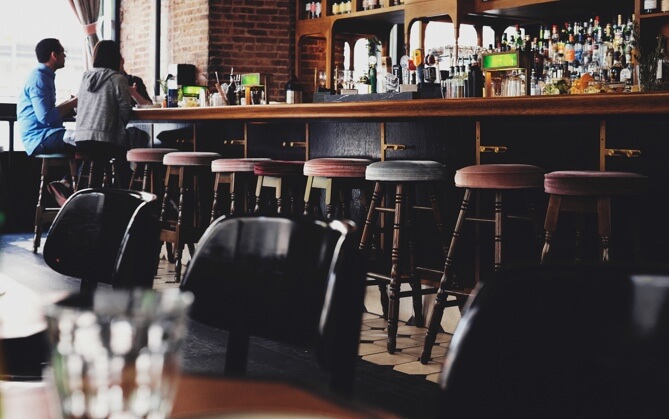 Another bar stocked with plenty of liquor. Three people are sitting on some of the bar's many stools.