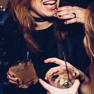 Two women laughing, holding cocktails.